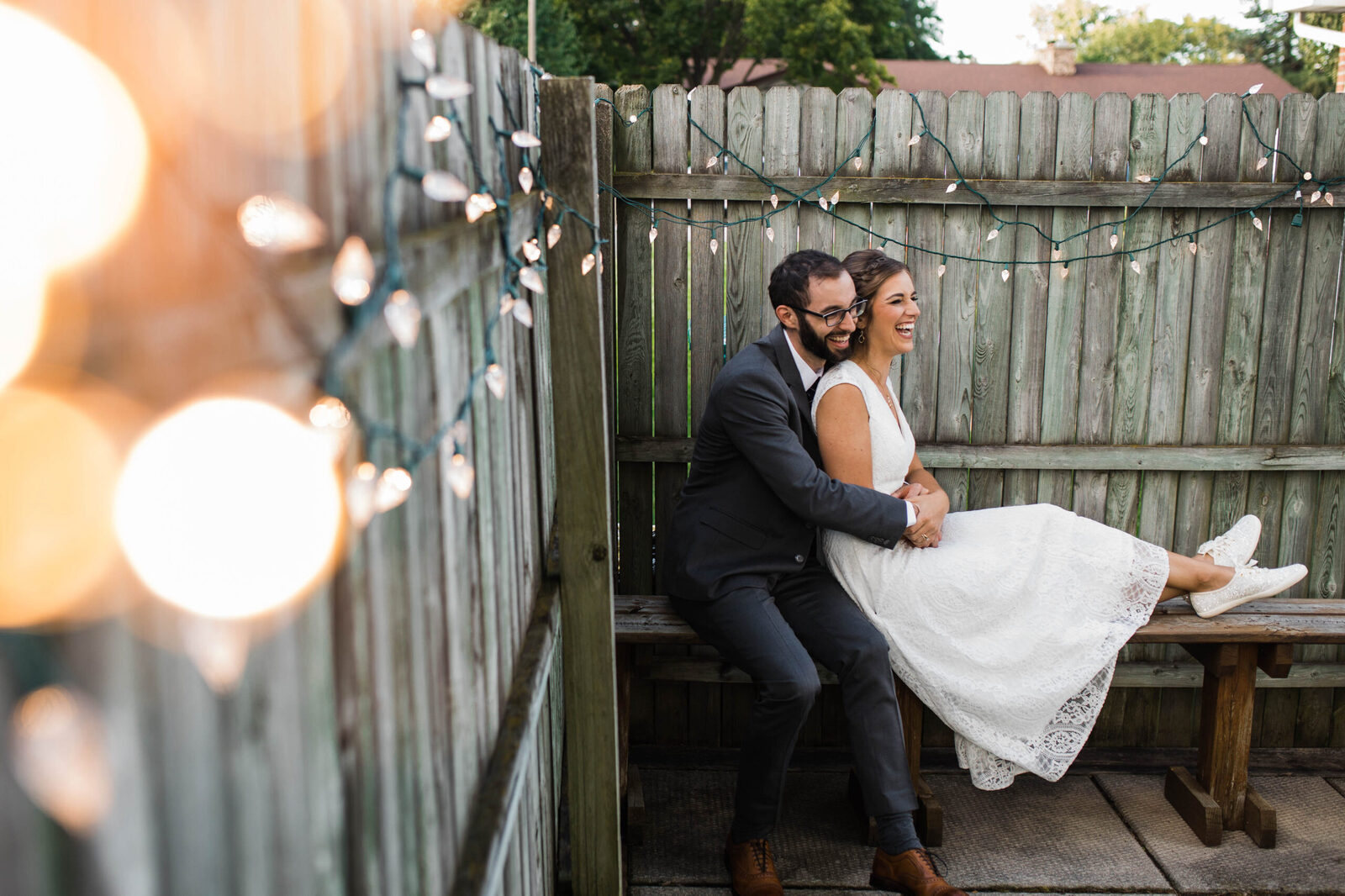 couple laughing by fence at their wedding reception